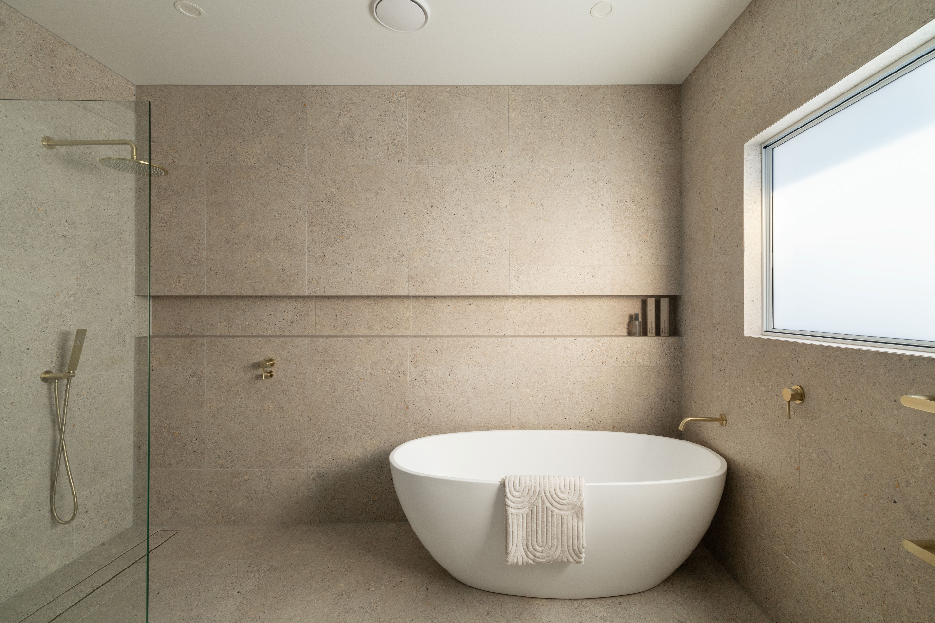 Minimal stone bathroom with freestanding bath and brass tapware