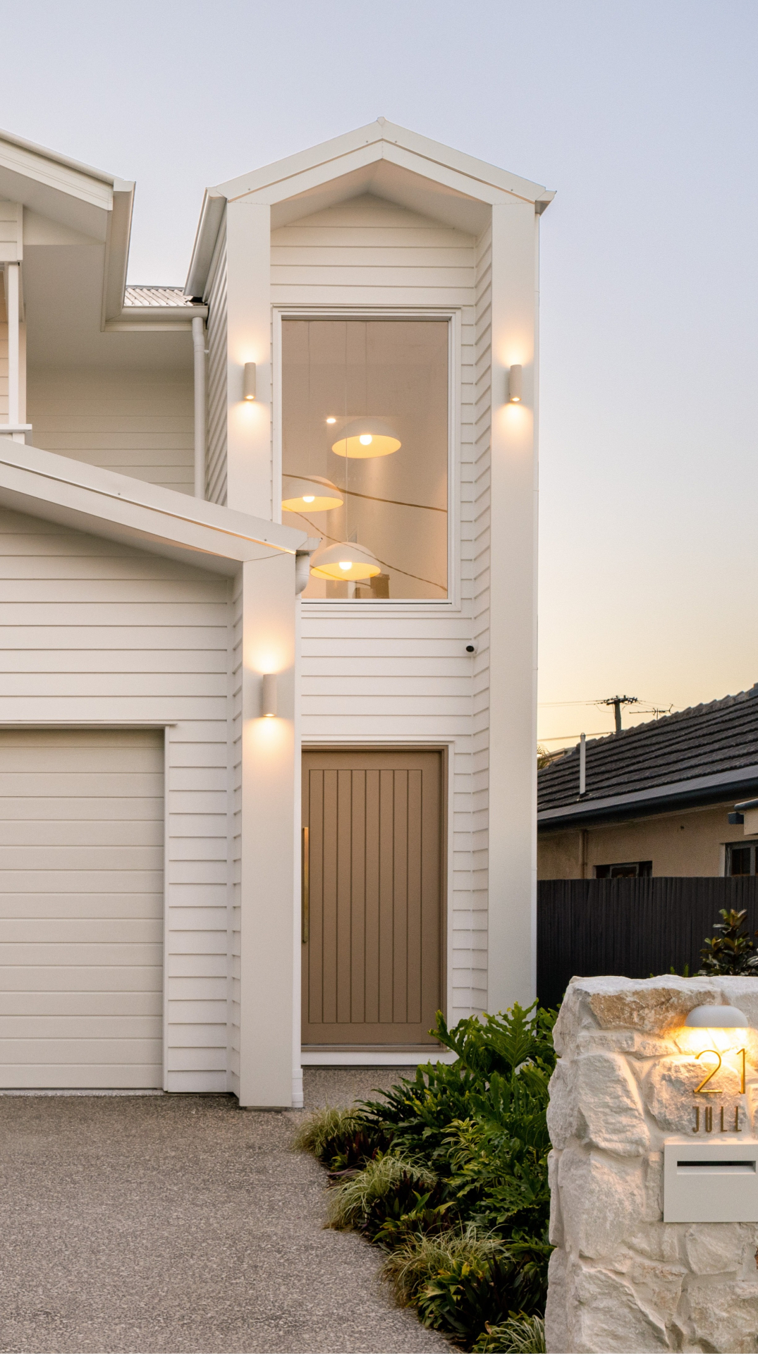 New-build coastal facade with double-height entry void at dusk, Geebung
