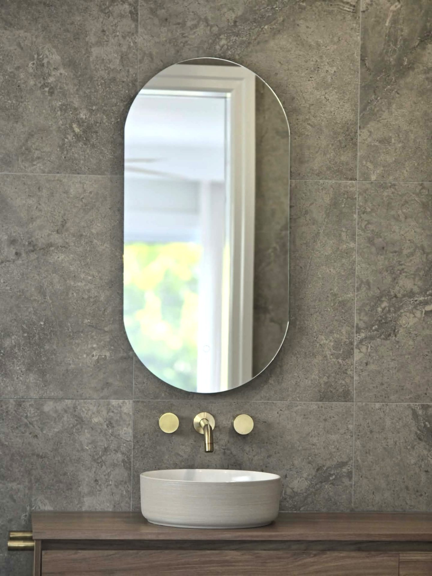 Grey stone-tiled ensuite with oval mirror and brass tapware